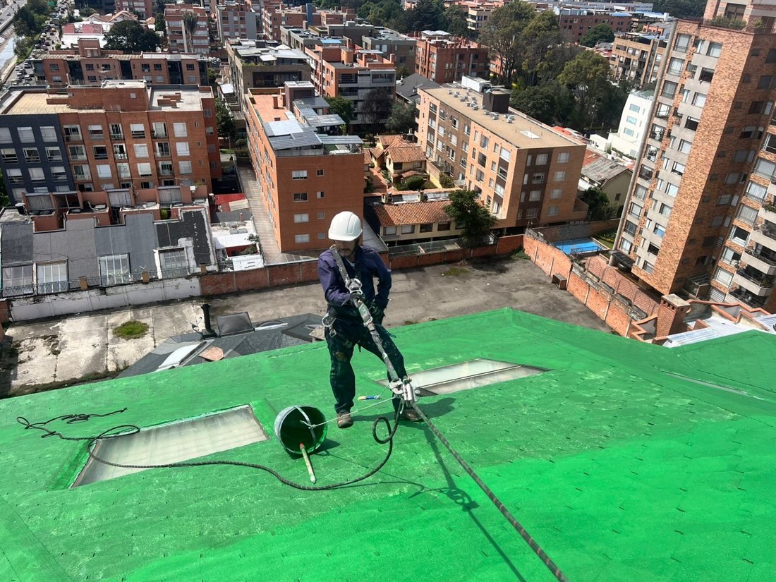 Técnico con arnés aplicando impermeabilizante en cubierta en altura