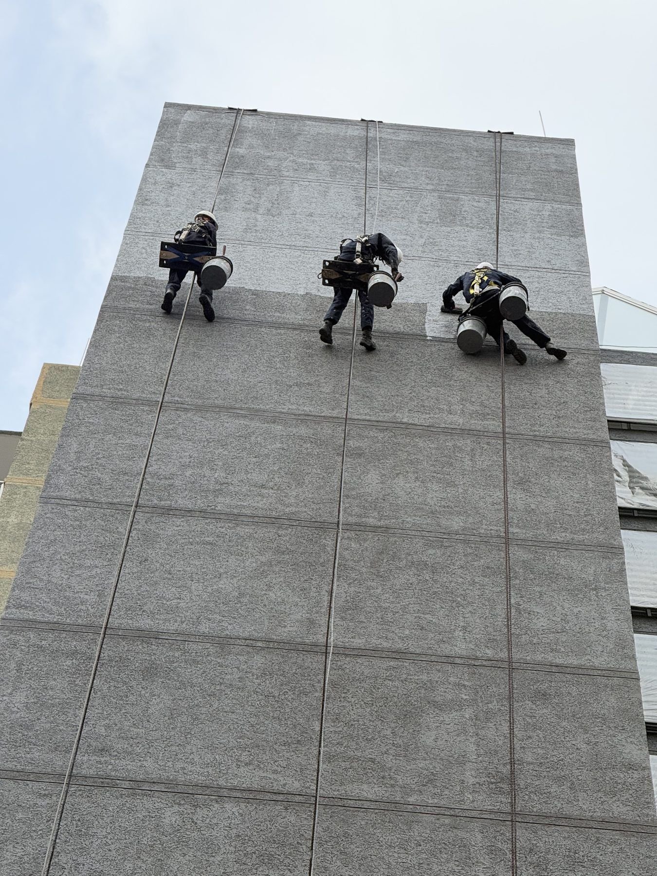 Equipo de técnicos en descenso aplicando impermeabilizante en fachada